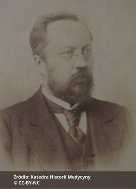 Fotografia czarno-biała przedstawiająca portret mężczyzny w okularach z wąsami i brodą, ubranego elegancko. Na dole zdjęcia napis "Źródło: Katedra Historii Medycyny oraz CC-BY-NC".