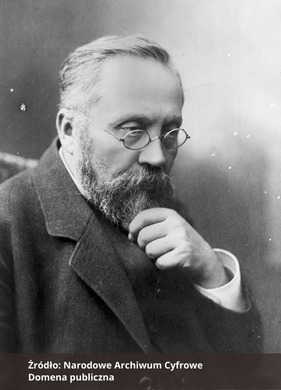 Czarno-biała fotografia portretowa mężczyzny z prawego profilu, z okularami, wąsami i brodą, ubranego elegancko,  Na dole zdjęcia podpis Źródło: Narodowe Archiwum Cyfrowe oraz Domena publiczna. 