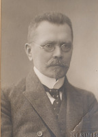 Ilustracja czarno-biała przedstawiająca mężczyznę w okularach z wąsami i brodą, ubranego elegancko, uchwyconego z prawnego profilu. 