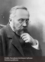 Czarno-biała fotografia portretowa mężczyzny z prawego profilu, z okularami, wąsami i brodą, ubranego elegancko,  Na dole zdjęcia podpis Źródło: Narodowe Archiwum Cyfrowe oraz Domena publiczna. 