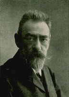 Czarno-biała fotografia na której znajduje się mężczyzna z wąsami i brodą, ubrany on jest elegancko, patrzącego na wprost.