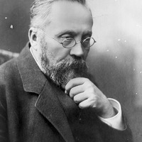 Czarno-biała fotografia portretowa mężczyzny z prawego profilu, z okularami, wąsami i brodą, ubranego elegancko,  Na dole zdjęcia podpis Źródło: Narodowe Archiwum Cyfrowe oraz Domena publiczna. 