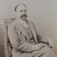 Fotografia czarno-biała przedstawiająca portret mężczyzny siedzącego na fotelu z wąsami, okularami, ubranego elegancko. Na dole zdjęcia napis "Źródło: Katedra Historii Medycyny i CC-BY-NC".