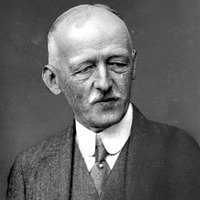 Fotografia czarno-biała przedstawiająca portret mężczyzny z wąsami ubranego elegancko. Na dole zdjęcia napis "Źródło: Narodowe Archiwum Cyfrowe oraz Domena publiczna".