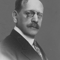 Fotografia czarno-biała przedstawiająca portret mężczyzny w okularach z wąsami i ubranego elegancko. Na dole zdjęcia napis "Źródło: Narodowe Archiwum Cyfrowe oraz Domena publiczna".